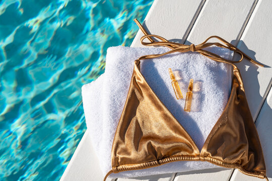 Golden bikini top and two vials of hair care oil on a white towel