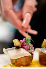 A close-up, shallow depth of field, food photograph of Nordic pickled herring canapés on mini potatoes, topped with red onion, dill, and yellow sauce, prepared by a chef.
