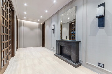 A hallway features a black marble fireplace and a large mirror on the wall. Wooden doors provide access to rooms. The space is well-lit with ceiling lights showing a modern design