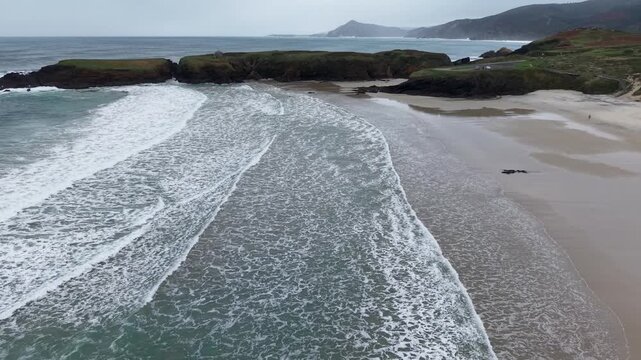 Ocean waves breaking on a sandy beach below a cloudy sky in ferrol, galicia