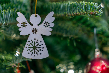 Decorative angel ornament hanging from Christmas tree branch with green needles and red bauble in the background