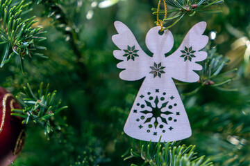Wooden angel ornament hangs from a Christmas tree branch decorated with green pine needles and red ball