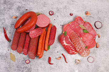 An assortment of various types of sausages, smoked meats, salami, and game sausages with lemon, spices, and herbs on a concrete table. Advertising and banner for a store, menu for a cafe or restaurant