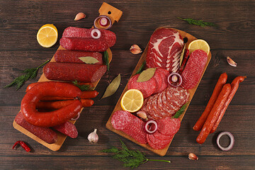 An assortment of various types of sausages, smoked meats, salami, and game sausages with lemon, spices, and herbs on a concrete table. Advertising and banner for a store, menu for a cafe or restaurant