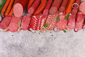 Delicious, aromatic appetizers of various salamis for the holidays. A selection of various smoked and dry-cured sausages and spices on a kitchen background. Advertising and menu for a store,