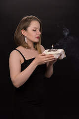 A woman in a black dress blows out a candle on a bento cake. Smoke on a black background. A girl's birthday, happiness, a gift. High quality photo
