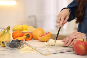 Woman cutting fruits for blending at white marble table indoors, closeup. Space for text