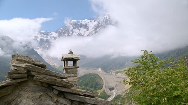 A stone roof with a chimney in the foreground and a mountain with glaciers and snow in the background. A stunning landscape of the Italian Alps with Monte Rosa at Macugnaga in the Anzasca Valley