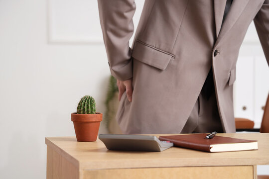 Young businessman with hemorrhoids and cactus on desk in office