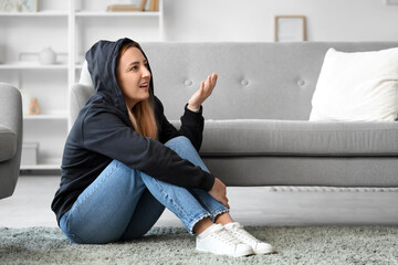 Angry mature woman in hoodie sitting at home. International Stress Awareness Week
