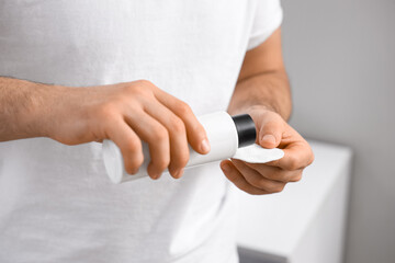 Handsome young man pouring micellar water on cotton pad in bathroom, closeup
