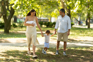 Fototapeta premium Family walking in park with newborn baby and toddler child