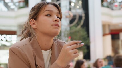young woman enhances appearance while shopping, fashionminded lady applies makeup amidst busy mall environment, enthusiastic female preparing her look during lively shopping experience