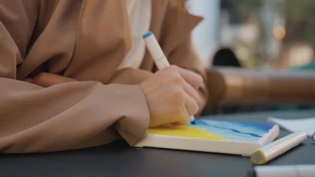 artist carefully creates precise forms on tiny canvas in warm environment, meticulous hand artist designs accurate patterns on miniature canvas using marker in comfortable indoor space