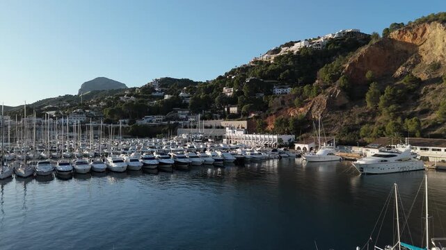 Javea Spain. Aerial drone video of the harbor with moored boats and sailboats, showing the town and beach in the background.