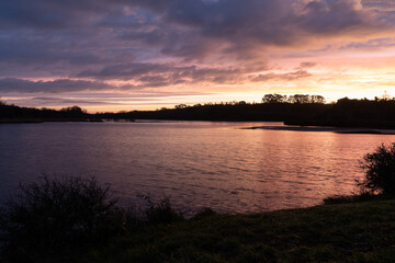 Lever de soleil calme sur l&rsquo;&eacute;tang de l&rsquo;Aber, sur la presqu&rsquo;&icirc;le de Crozon en Bretagne, avec des nuages doux se refl&eacute;tant sur l&rsquo;eau et une atmosph&egrave;re paisible.