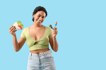 Young African-American woman with tasty taco and maracas on blue background