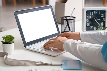 Female doctor working with laptop at table in clinic, closeup