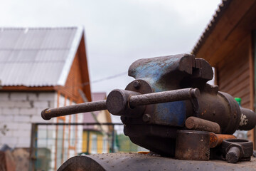 Working metal vise in a workshop by wooden buildings on a cloudy day