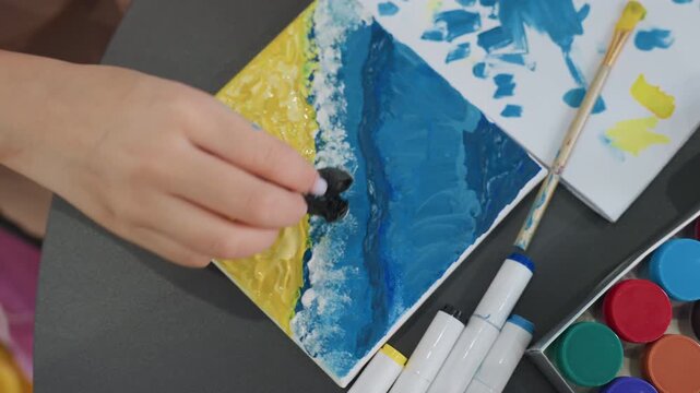 hands paint shoreline, female hands dab blue paint to craft shoreline details on small canvas, closeup of female hands applying dark blue paint to depict shoreline texture with sponge