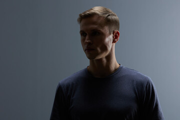 thoughtful man in shadow dark moody portrait wearing dark t-shirt looking down on black background...