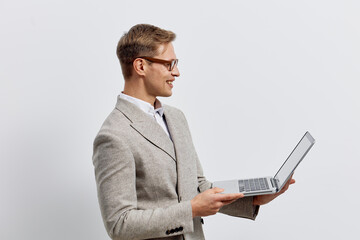 Smiling man wearing glasses and light gray blazer holding open laptop computer, looking at screen...