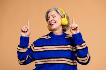 Aged mature woman dancing with yellow headphones wearing a blue striped knit sweater smiling in a...