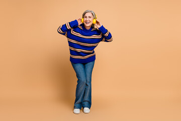 Senior woman wearing a blue striped knit sweater listens to music with yellow headphones smiles in...