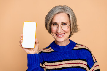 Caring elderly mature woman holding a smartphone and smiling in a blue striped knitwear against...