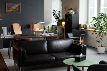 Empty modern therapy office showing organized workspace with desk, books, plants and comfortable seating area, suggesting professional environment for counseling or mental health sessions