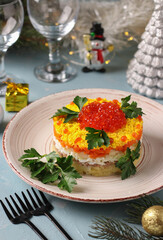 Festive puff salad Mimosa with canned fish, potatoes, cheese, carrots and eggs, garnished with red caviar and parsley leaves