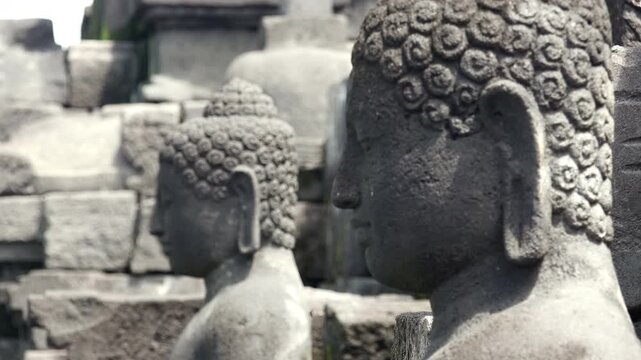 Heads of stone statues of meditating Buddha illuminated by sun at Borobudur Buddhist temple in Magelang, Central Java, Indonesia. Sanctuary decoration. Focus switches from background to foreground.