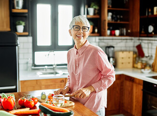 Fototapeta premium Portrait of happy senior mid aged mature woman prepering meal with fresh vegatebles in kitchen at home