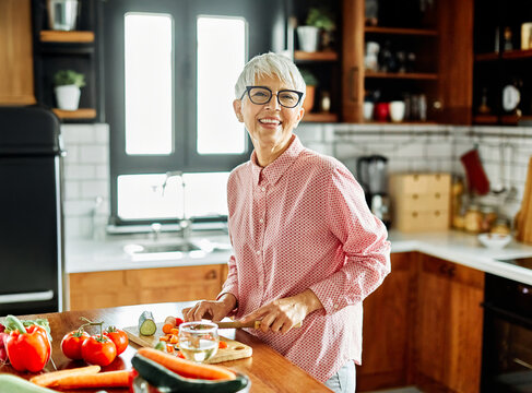 Portrait of happy senior mid aged mature woman prepering meal with fresh vegatebles in kitchen at home