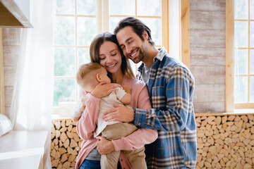 Parenthood and child care. Parent`s nurturing. Happy young family, mother and father hugging embracing little small child kid toddler at home kitchen. Insurance mortgage for people