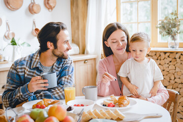 Morning breakfast at home. Young caucasian family of three, parents and infant toddler new born...