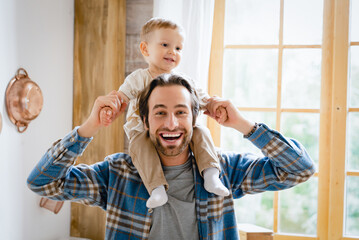 Happy young caucasian father dad playing piggyback with little small kid child toddler infant, spending time together. Baby care and parenthood, fatherhood concept.