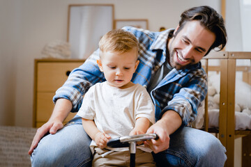 Young caucasian father dad playing spending time with little son kid child toddler baby infant on toy car bicycle at home. Parenthood and fatherhood concept. Child developing games