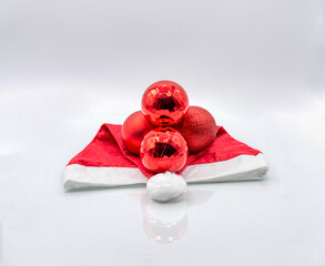 Santa Claus hat and four red Christmas tree ornaments on a white background