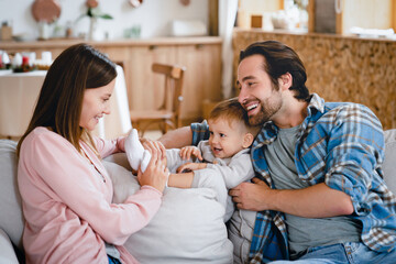 Child home care. Caucasian young family parents taking care of little toddler together, relaxing on the couch at home, nurturing and spending family time. Parenthood concept