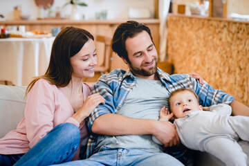 Young caucasian mother and father parents taking care of their toddler son small little daughter kid child at home, relaxing on the sofa together. Parenthood concept. Family time