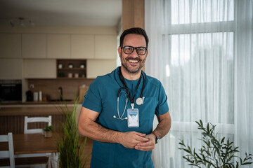 Happy male doctor wearing scrubs and stethoscope, standing indoors
