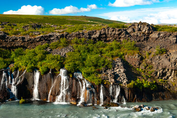 Hraunfossar is a unique Icelandic waterfall in West Iceland where clear, cold spring water seeps directly from under the Hallmundarhraun lava field, forming hundreds of small, delicate waterfalls.