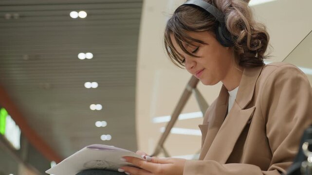 young woman sketching with headphones, young lady concentrating on drawing and annotating routes silently, female artist absorbed in sketching and jotting notes under focused lighting conditions