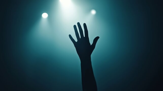 Reaching for hope a hand raised in the dark emotional concert moment indoor venue dramatic lighting artistic perspective