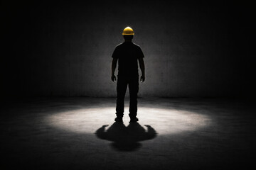 Obraz premium The Lone Worker in Spotlight: A construction worker stands centered in a solitary space. The image evokes themes of individual work in a dark room.