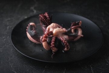 Hot prepared squid or boiled octopus with tentacles wiggling on a plate with steam coming out against black background. Seafood background for a restaurant menu © alexanderon