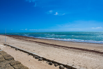 Wide sandy beach with calm sea and blue sky, coastal city on the horizon creating a peaceful seaside landscape with copy space.
