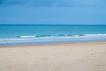 Wide sandy beach with calm sea and blue sky, coastal city on the horizon creating a peaceful seaside landscape with copy space.