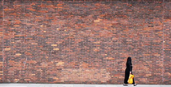 A woman walks past a very large wall.